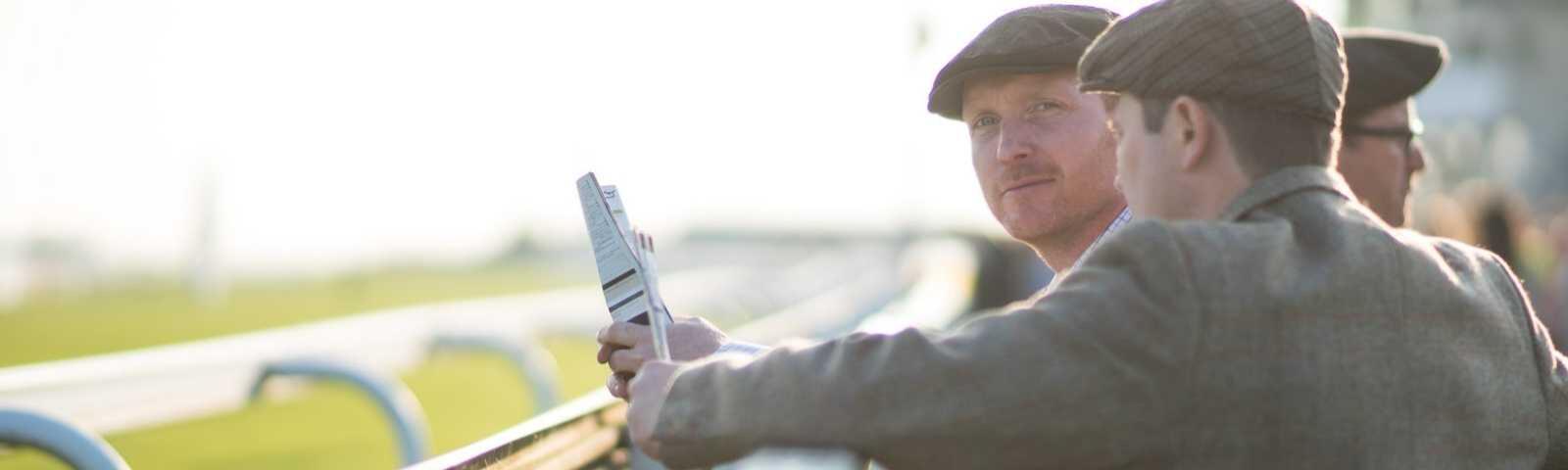 Well-dressed racegoers watch the horse racing from the running rail
