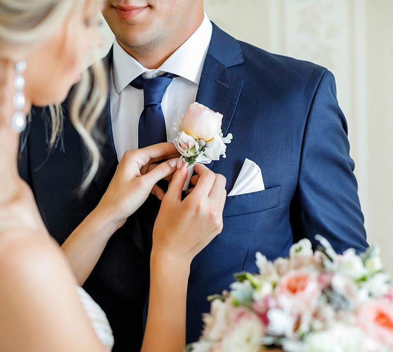 A bride pinning a flower to her grooms jacket.